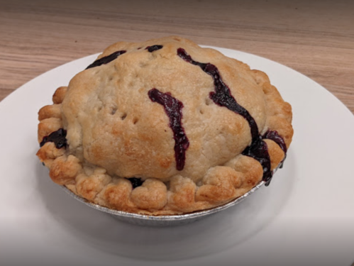 A freshly baked pie with a golden crust and berry filling, sitting on a white plate against a wooden background.