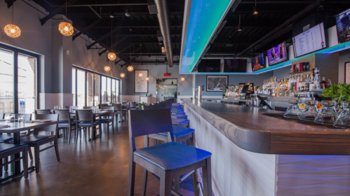 Modern restaurant interior featuring a sleek bar, high stools, and large windows with ambient lighting.