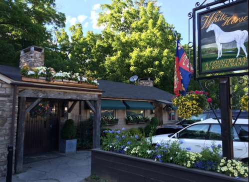 Exterior of the White Horse Country Pub & Restaurant, featuring a sign, flowers, and a stone entrance.