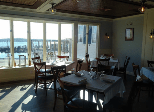 Bright restaurant interior with tables set for dining, large windows overlooking a waterfront view.