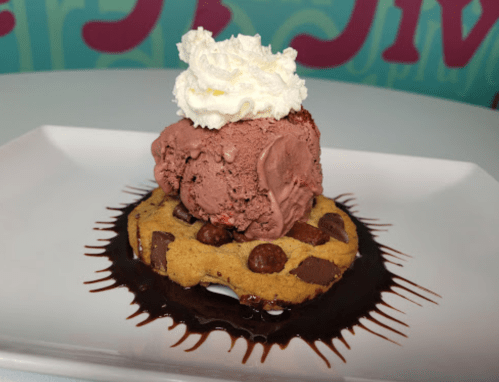 A chocolate chip cookie topped with chocolate ice cream and whipped cream, drizzled with chocolate sauce.