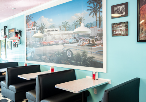 A retro diner interior with black booths, a large mural of classic cars, and vintage decor on the walls.