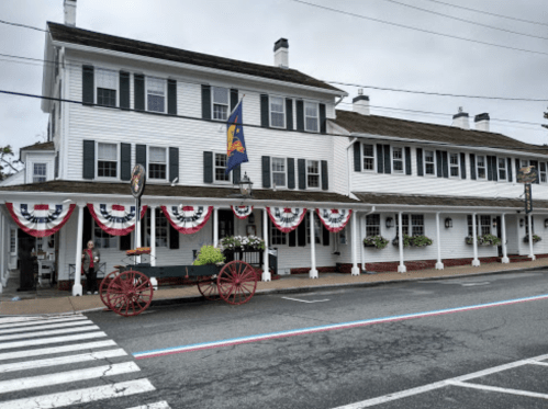 Historic building with white siding, decorative bunting, and a horse-drawn carriage in front on a cloudy day.