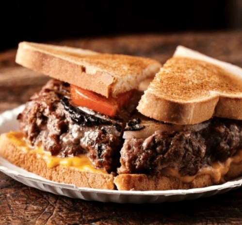 A hearty burger with melted cheese, tomato, and grilled onions, served between two slices of toasted bread.