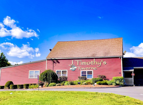 Exterior of J. Timothy's Taverne, a red building with a sloped roof, surrounded by green landscaping and a blue sky.