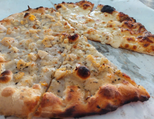 Close-up of two slices of pizza with a golden crust, topped with cheese and chunks of chicken.