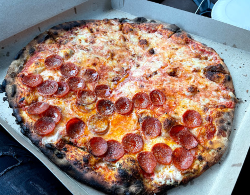 A large pepperoni pizza with a crispy crust, placed in a pizza box.