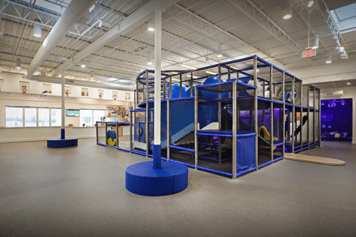 Indoor play area featuring a large, colorful climbing structure with slides and tunnels, surrounded by open space.
