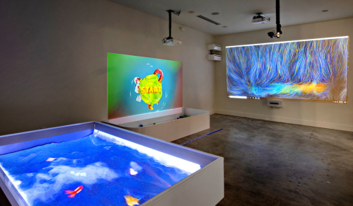 A modern room with a digital projection on the wall and a blue sand-filled area, creating an interactive environment.