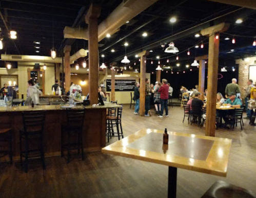 A lively restaurant interior with wooden beams, tables, and patrons enjoying food and drinks. Warm lighting creates a cozy atmosphere.