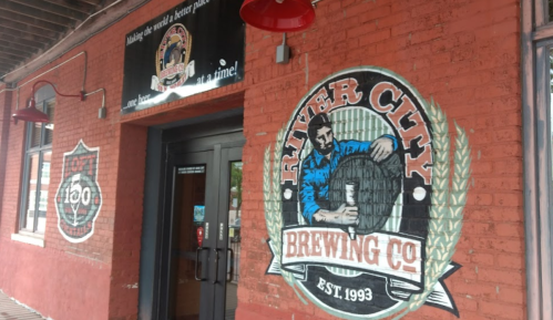 Exterior of River City Brewing Co. featuring a red brick wall with murals and a sign above the entrance.