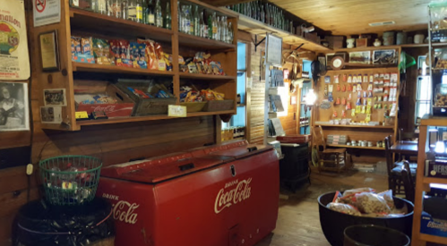 A vintage store interior featuring a red Coca-Cola cooler, shelves of snacks, and rustic wooden decor.