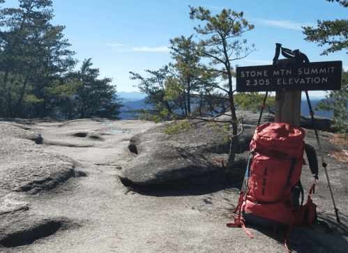 A red backpack rests on rocky terrain near a sign marking the Stone Mountain Summit at 2,305 feet elevation.