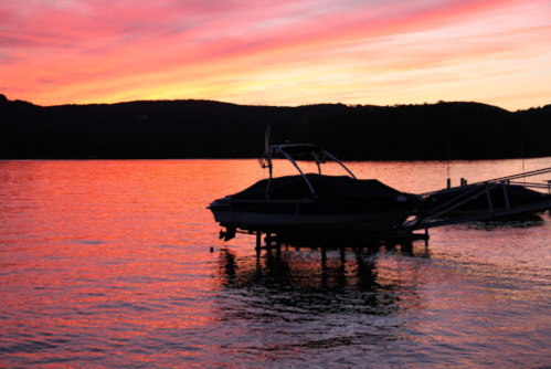 A serene sunset over a lake, with a silhouette of a boat on a dock and vibrant pink and orange skies.