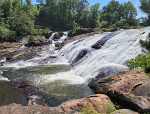 A scenic waterfall cascading over rocky terrain, surrounded by lush green trees under a clear blue sky.