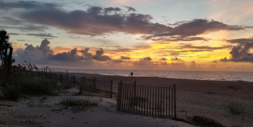 A serene beach at sunset, with vibrant clouds and two people walking along the shore.