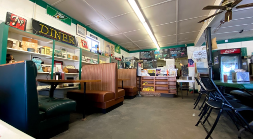 Interior of a diner featuring booths, shelves with vintage items, and a menu board in a cozy, nostalgic setting.