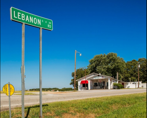 A roadside view featuring a "Lebanon" street sign and a small store under a clear blue sky.