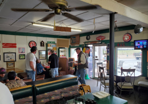 A cozy diner interior with patrons chatting, vintage decor, and a fan overhead, creating a welcoming atmosphere.