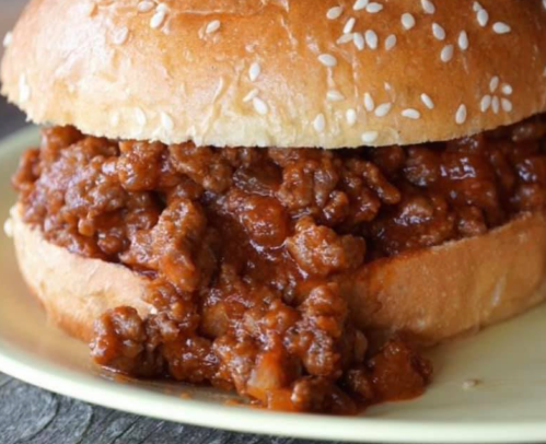 A close-up of a sesame seed bun filled with a savory, thick meat mixture.