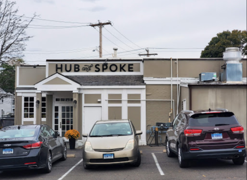 Exterior of a building labeled "Hub and Spoke," with parked cars in front and a clear sky above.