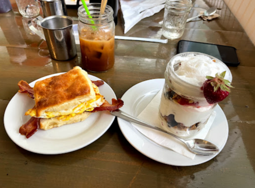A breakfast plate with a bacon and egg sandwich and a parfait with yogurt, granola, and a strawberry on top.