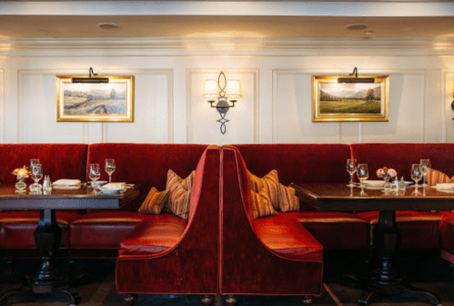 Cozy restaurant interior with red booths, elegant table settings, and framed landscape paintings on the walls.