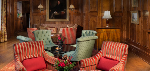 Cozy living room with striped chairs, a coffee table, and wooden paneling, featuring a large portrait on the wall.