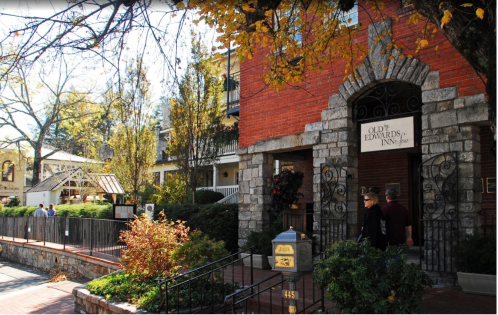 Historic brick building with a sign reading "Old Edwards Inn," surrounded by autumn foliage and visitors.