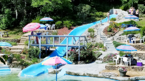 A colorful water slide in a lush garden setting, with umbrellas and people enjoying the area.