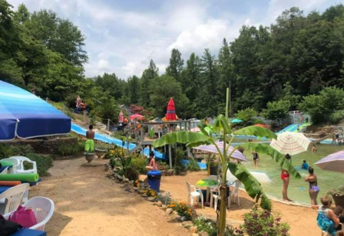 A vibrant water park scene with slides, umbrellas, and people enjoying the water amidst lush greenery.