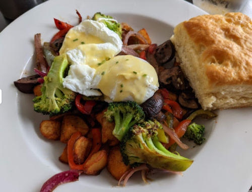 A plate of colorful sautéed vegetables topped with poached eggs and a biscuit on the side.