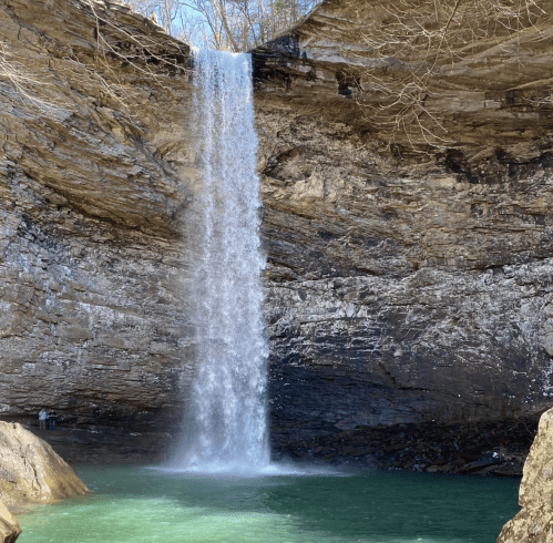 A waterfall cascades down rocky cliffs into a serene turquoise pool below, surrounded by bare trees.