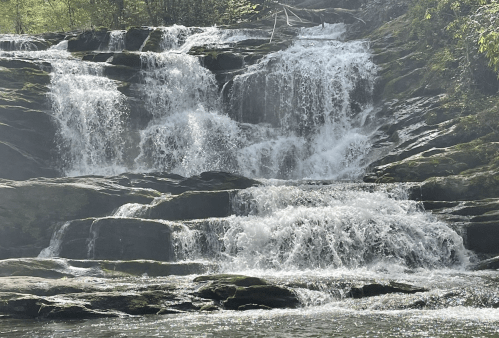 A serene waterfall cascading over rocky steps, surrounded by lush greenery and mist.