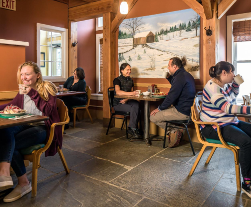 A cozy café scene with four people enjoying food and drinks, surrounded by a winter-themed mural.