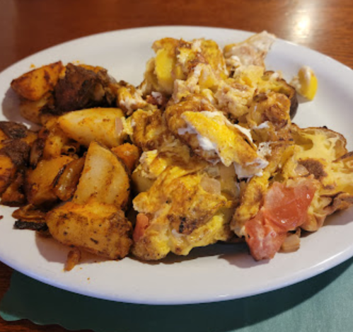 A plate of scrambled eggs mixed with tomatoes, served alongside seasoned roasted potatoes.