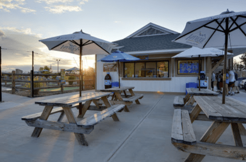Outdoor seating area with wooden picnic tables and umbrellas, near a food stand at sunset.