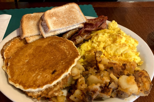 A hearty breakfast plate with pancakes, scrambled eggs, bacon, sausage, toast, and hash browns.