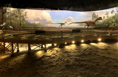 A museum exhibit featuring a prehistoric landscape with dinosaurs and a curved display platform.