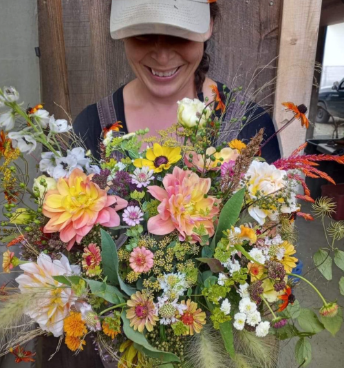 A person holding a vibrant bouquet of mixed flowers, smiling against a rustic wooden background.