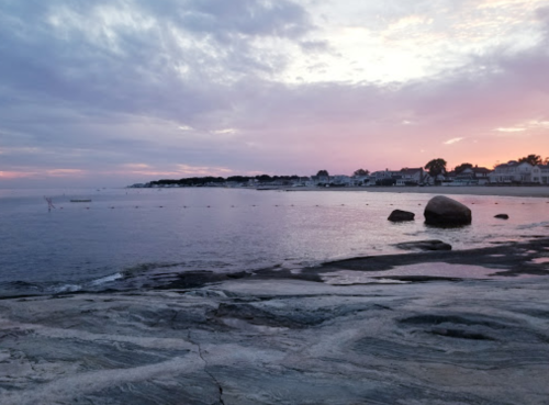 A serene coastal scene at sunset, featuring calm waters, rocky shorelines, and a pastel sky.