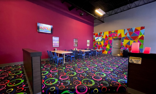 Brightly colored interior of a fun venue with a vibrant carpet, tables, and a colorful wall design.