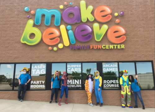 A colorful sign reads "Make Believe Family Fun Center," with staff in costumes posing outside the building.