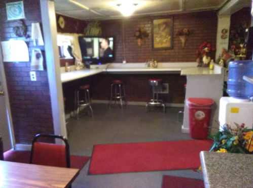 Cozy kitchen with a bar area, red stools, a TV, and decorative plants against a brick wall.