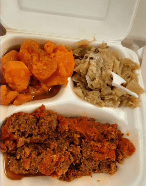 A takeout container with sweet potatoes, cabbage, and a serving of meatloaf with sauce.