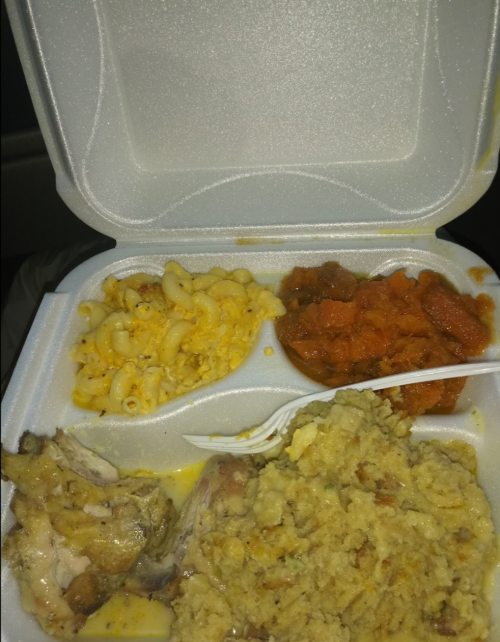 A takeout container with macaroni and cheese, sweet potatoes, stuffing, and a piece of chicken.