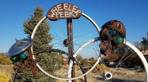 A whimsical bike sculpture with vintage lights and a sign reading "Wheeler Peak" against a clear blue sky.