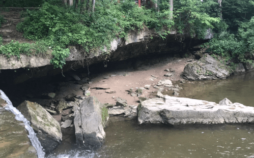 A serene river scene with rocky banks, lush greenery, and a small waterfall cascading into the water.