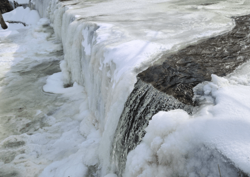 A frozen waterfall with ice and snow surrounding the flowing water, creating a serene winter landscape.