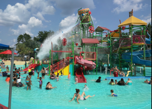 A vibrant water park with slides and play structures, filled with families enjoying the water on a sunny day.